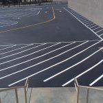 Freshly painted car park with bright white line markings and directional arrows on a smooth black asphalt surface, providing clear parking spaces and traffic guidance.